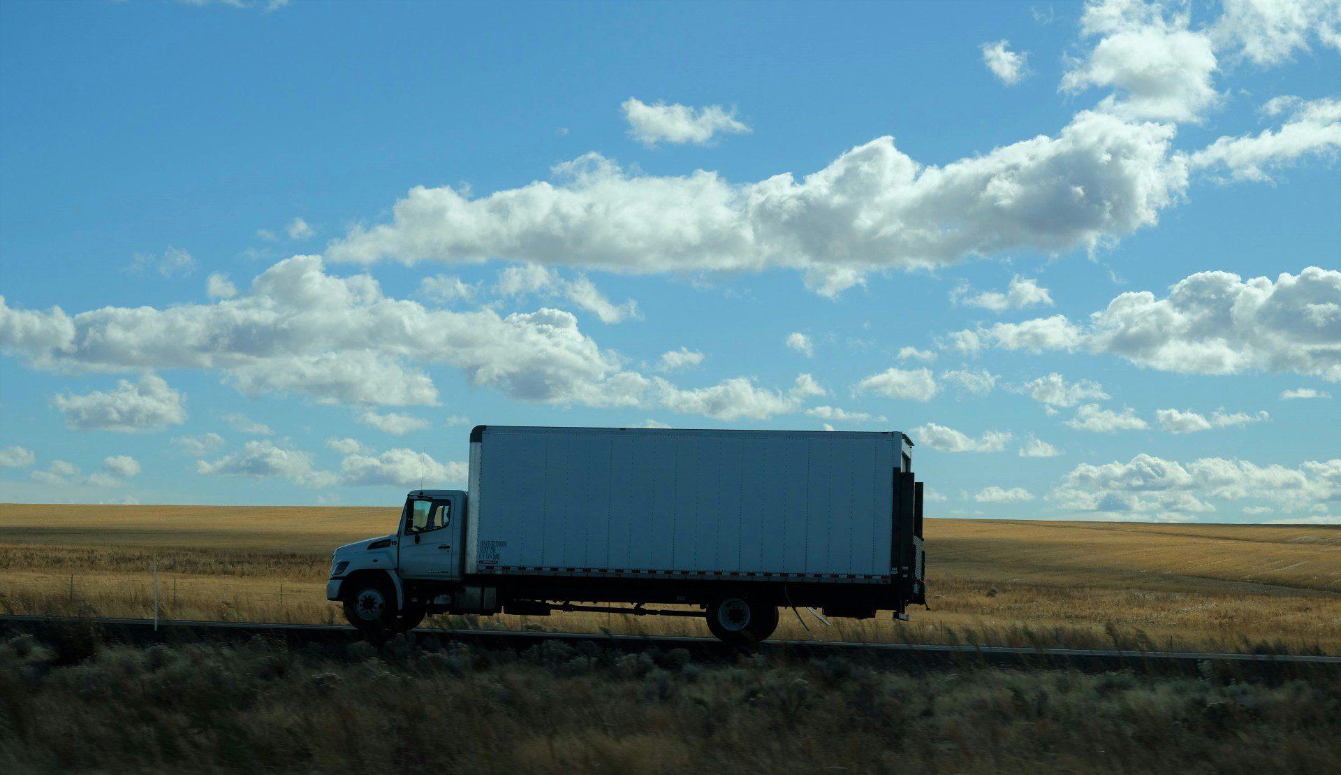 A blue semi-truck parked on a grassy field under a partly cloudy sky.