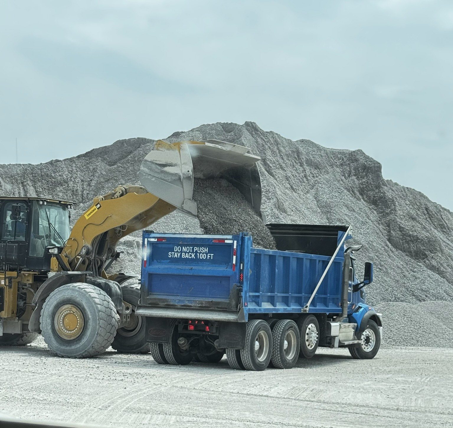 A blue dump truck and yellow excavator at a quarry site.